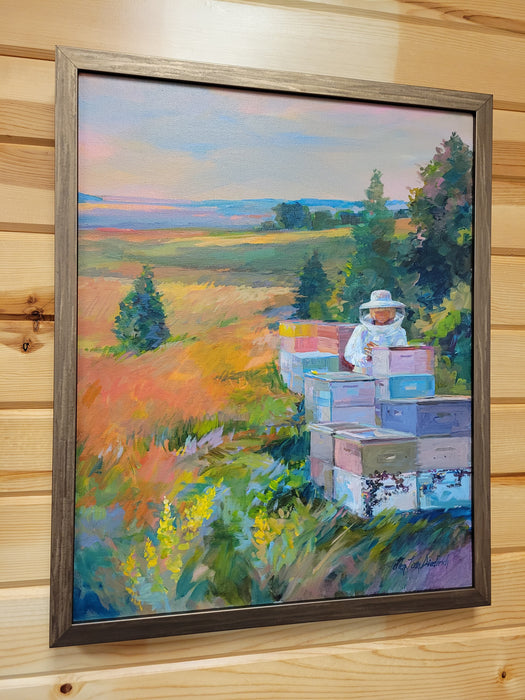 A framed landscape painting of a beekeeper working with beehives in a field, displayed on a light wood-paneled wall.