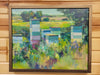 A framed landscape oil painting depicting beehives in a field, mounted on a light wood paneled wall. The painting features green, blue, and yellow tones with a dark brown wooden frame.